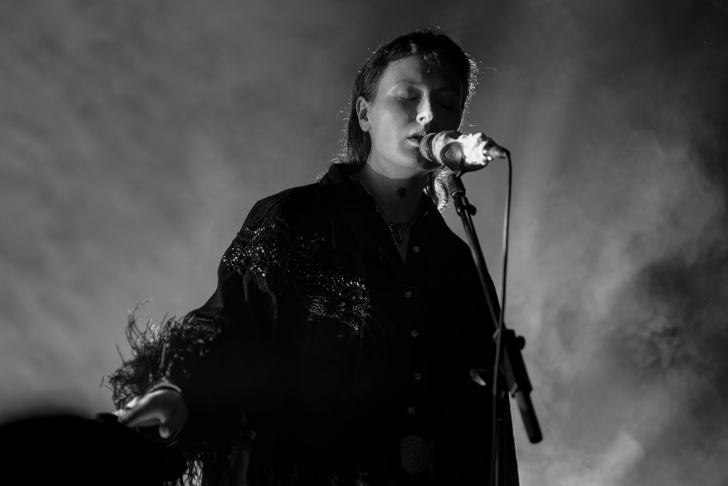 Singer performing on stage with a microphone, surrounded by dramatic lighting and smoke.