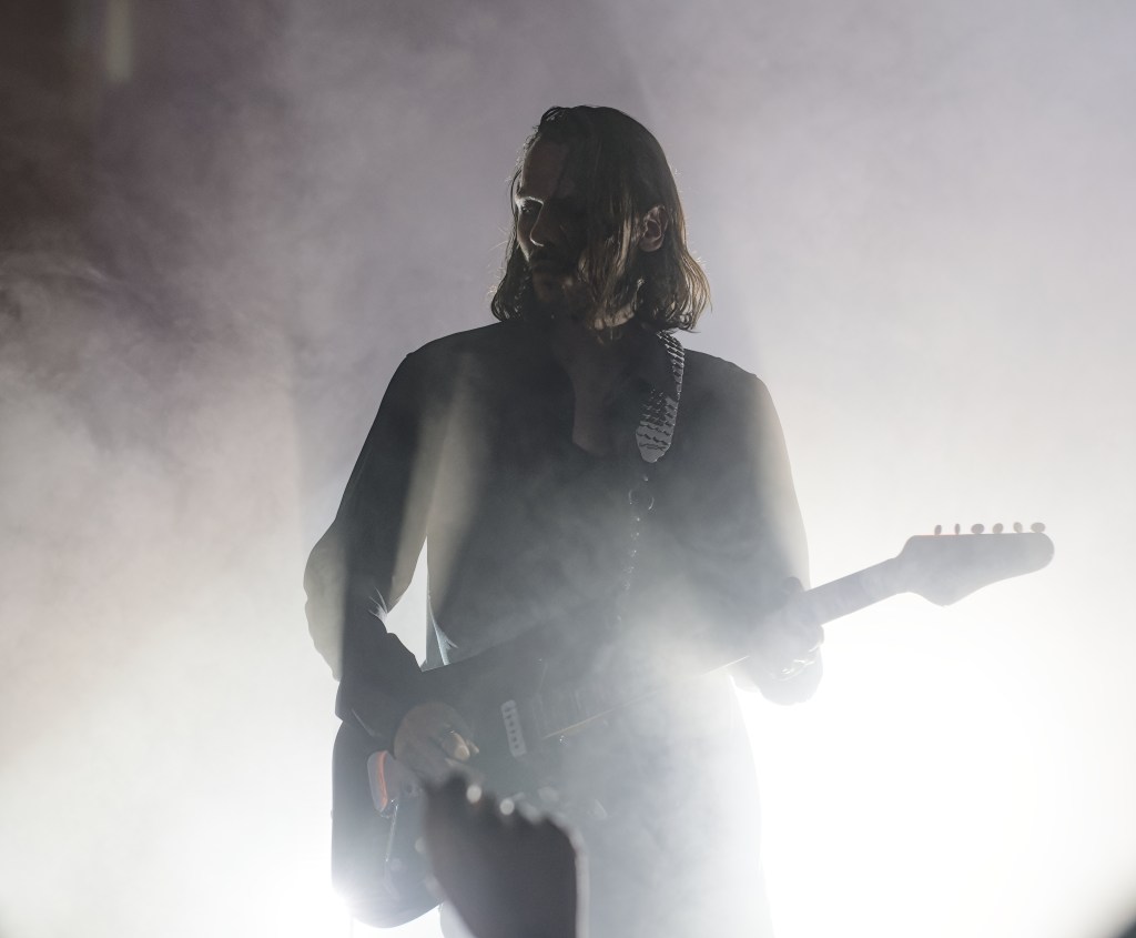A guitarist performing on stage shrouded in smoke, with soft lighting creating a dramatic silhouette.