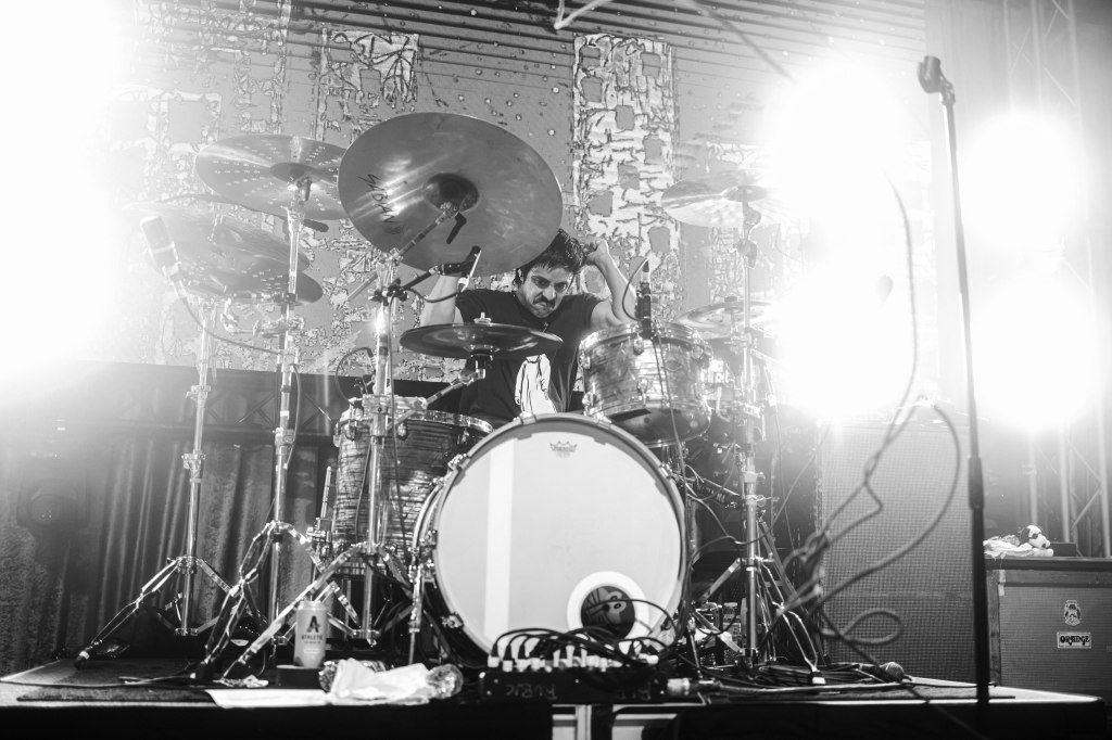 Drummer performing on stage with intense lighting and vibrant energy.