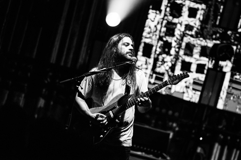 Musician playing guitar on stage with dramatic lighting in black and white.