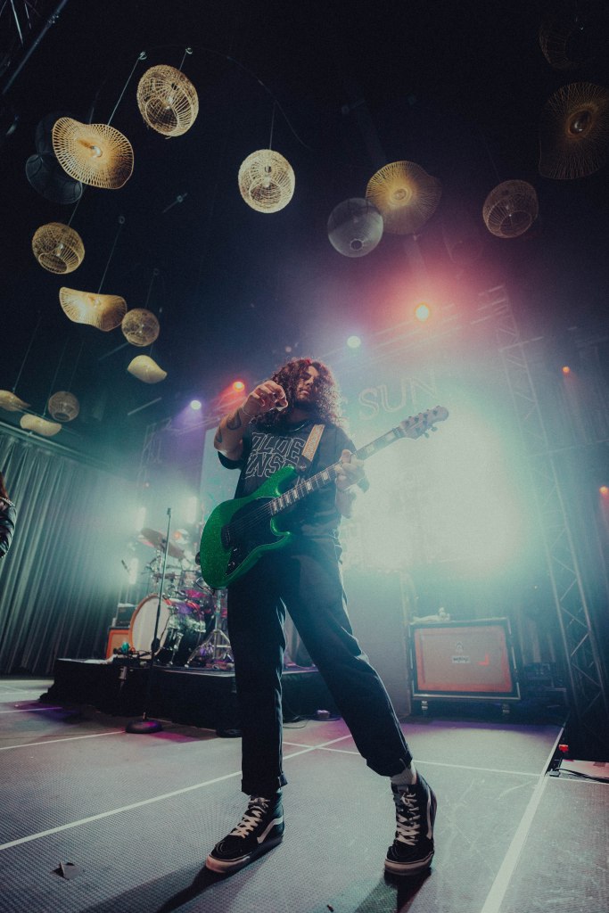 A musician performing on stage, playing a green electric guitar with a lively atmosphere and colorful lighting.