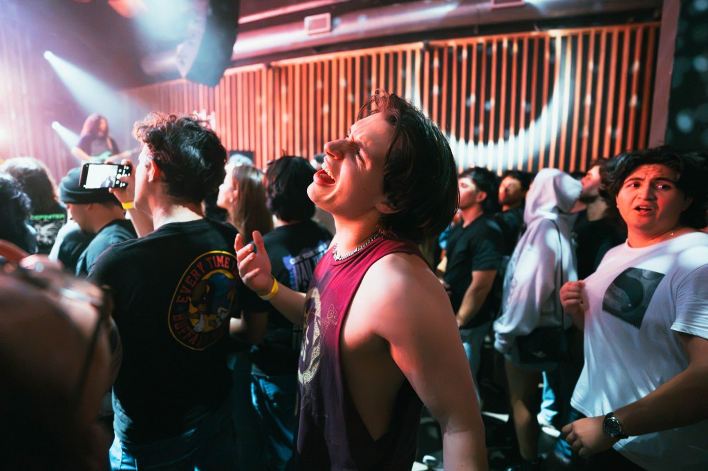 A crowd of enthusiastic concertgoers enjoying a live performance, with one person in the foreground singing passionately.
