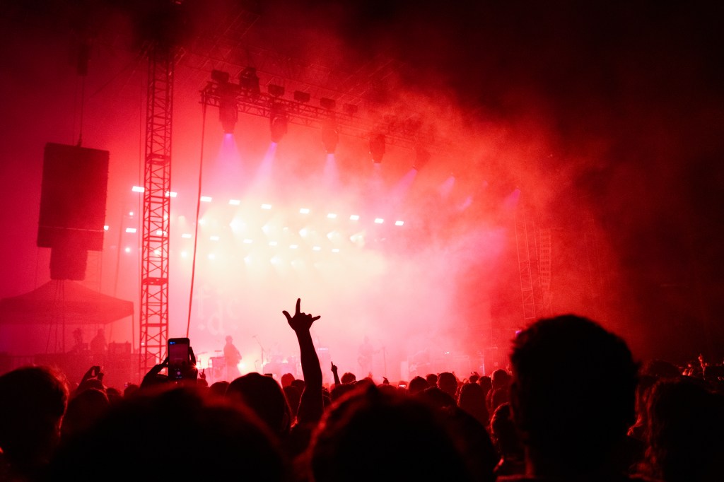 Crowd at a concert with red lighting and fog, silhouetted figures enjoying the performance.