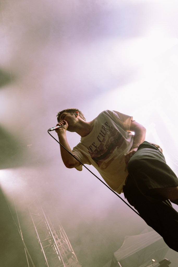 A singer performing on stage with a microphone, surrounded by dramatic lighting and smoke during a concert.