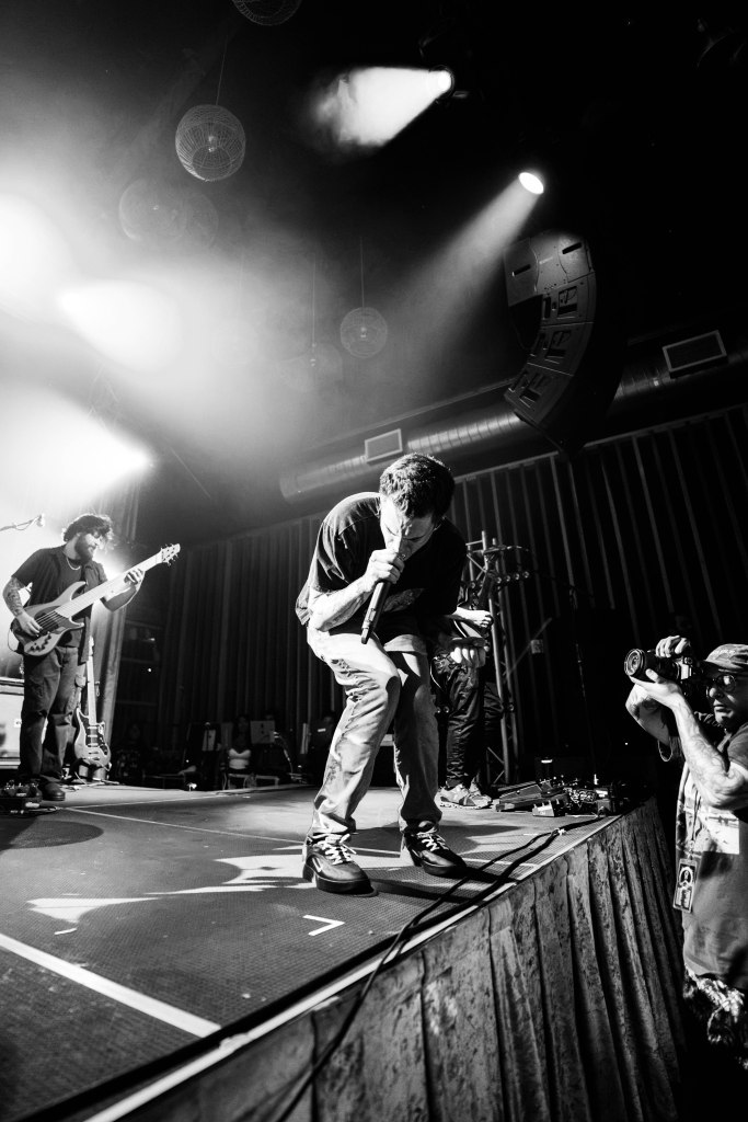 A singer performing passionately on stage with a microphone, surrounded by band members and focused spotlights.