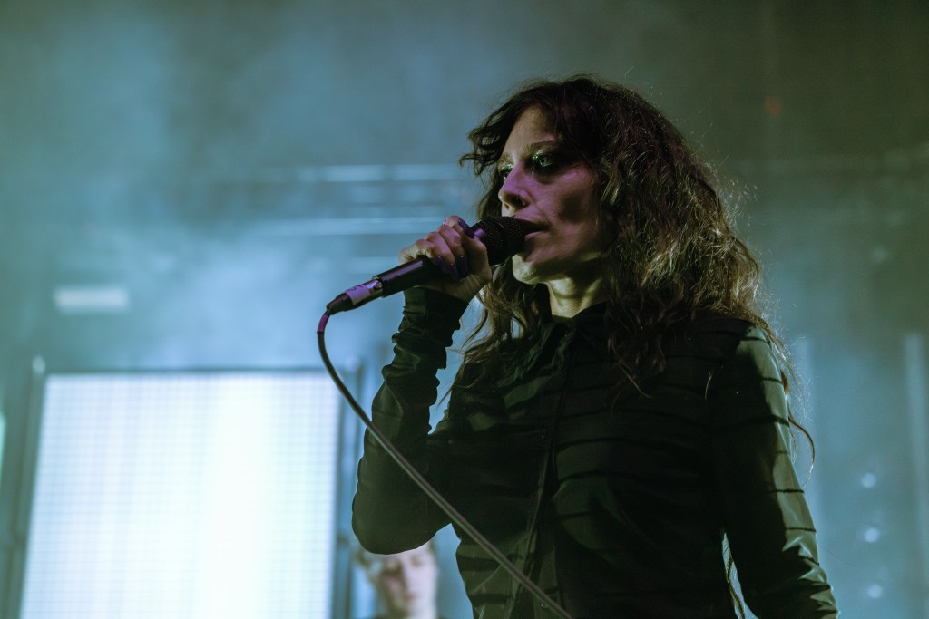 A singer performing on stage with a microphone, surrounded by fog and dramatic lighting.