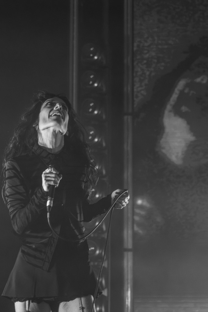 A female singer passionately performing on stage with a microphone, wearing a black outfit and surrounded by dramatic lighting.