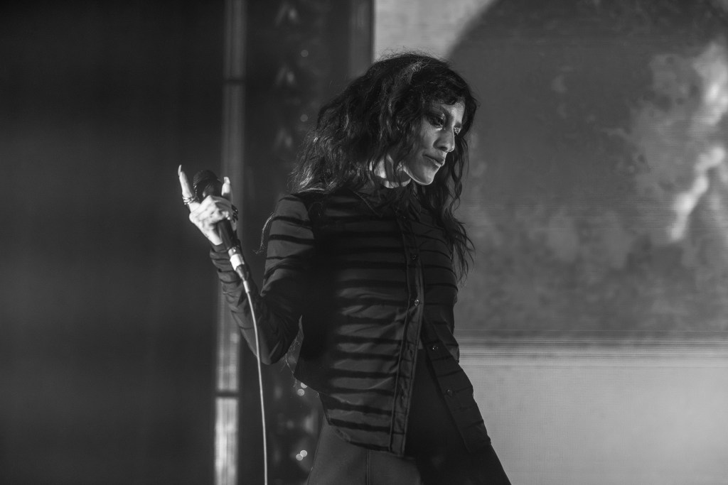 A black and white image of a female singer on stage, holding a microphone, with a thoughtful expression and dramatic lighting.