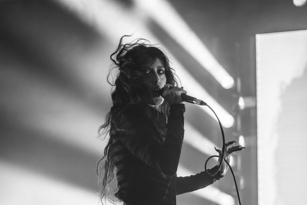 A female singer performing on stage with a microphone, illuminated by dramatic lighting in black and white.