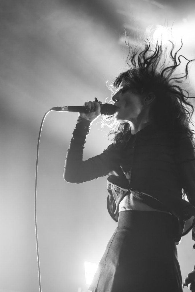 A singer performing passionately on stage with dynamic hair movement and holding a microphone, surrounded by dramatic lighting.