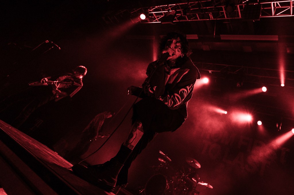 A musician performing passionately on stage with dramatic lighting, surrounded by bandmates playing instruments.