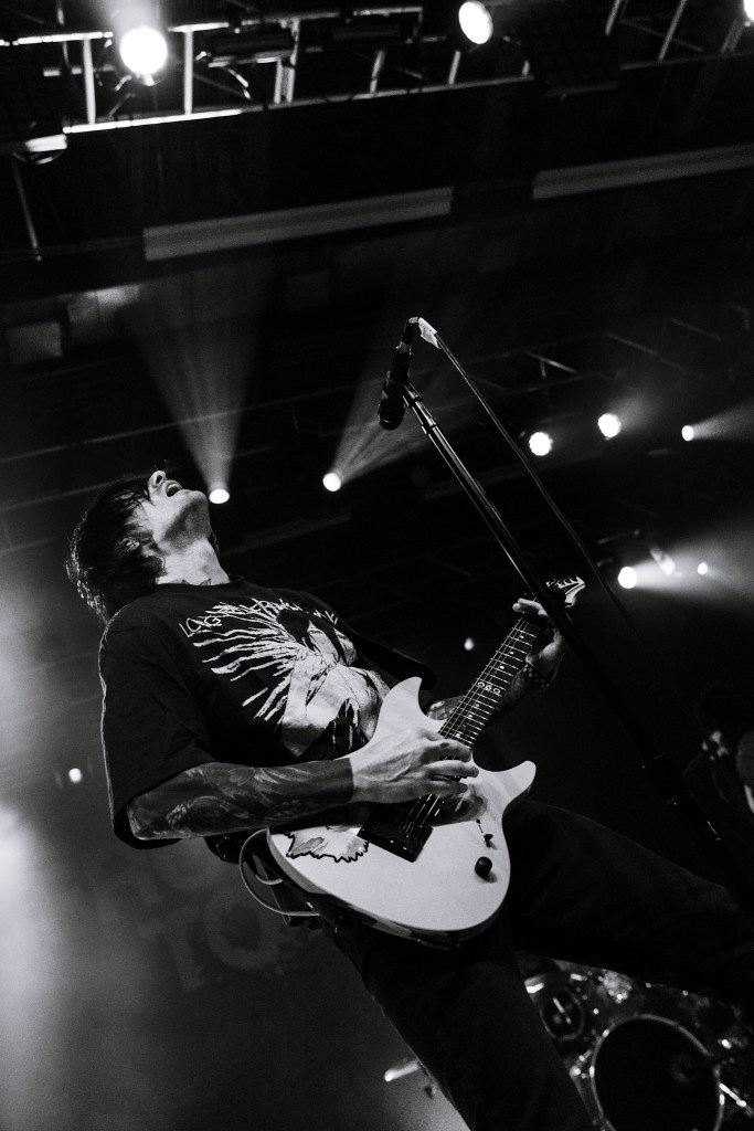 A musician performing on stage, passionately playing an electric guitar while looking upwards, with dramatic lighting and a black and white color scheme.