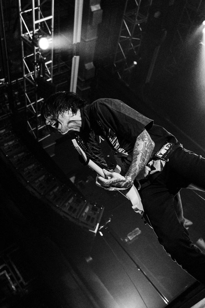 A musician passionately playing an electric guitar on stage, captured in black and white.