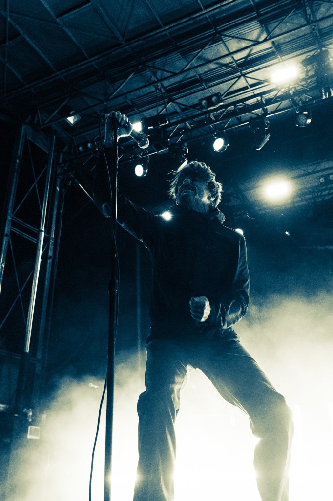 A singer performing on stage with a microphone, illuminated by dramatic lighting and surrounded by fog.