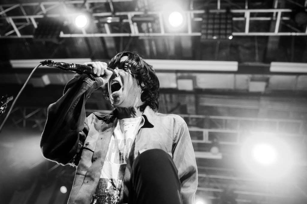 A black and white image of a male singer passionately performing on stage, holding a microphone and singing, with bright lights illuminating the background.