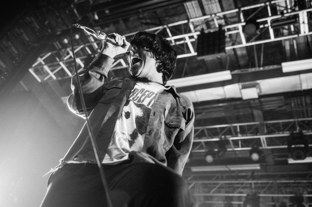 A singer passionately performing on stage, holding a microphone and engaging with the audience, captured in a black and white format.