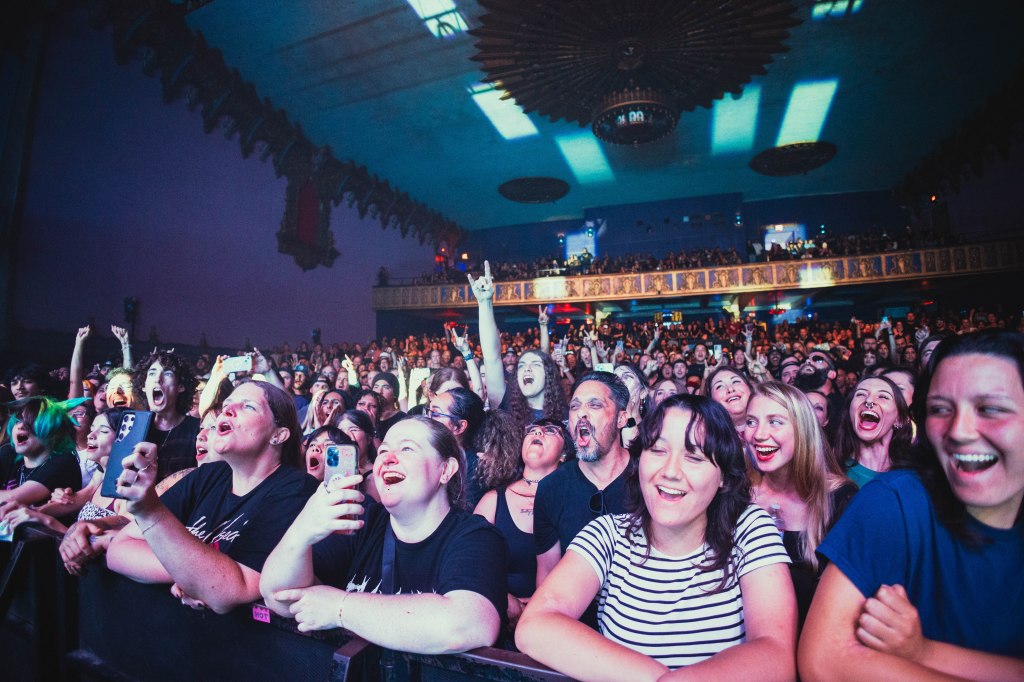 A lively crowd of fans at a concert, cheering and enjoying the performance, with mixed expressions of excitement and joy.