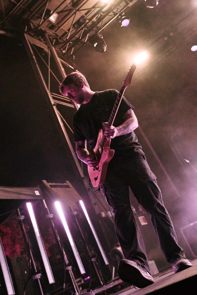 A musician playing an electric guitar on stage under dramatic lighting.