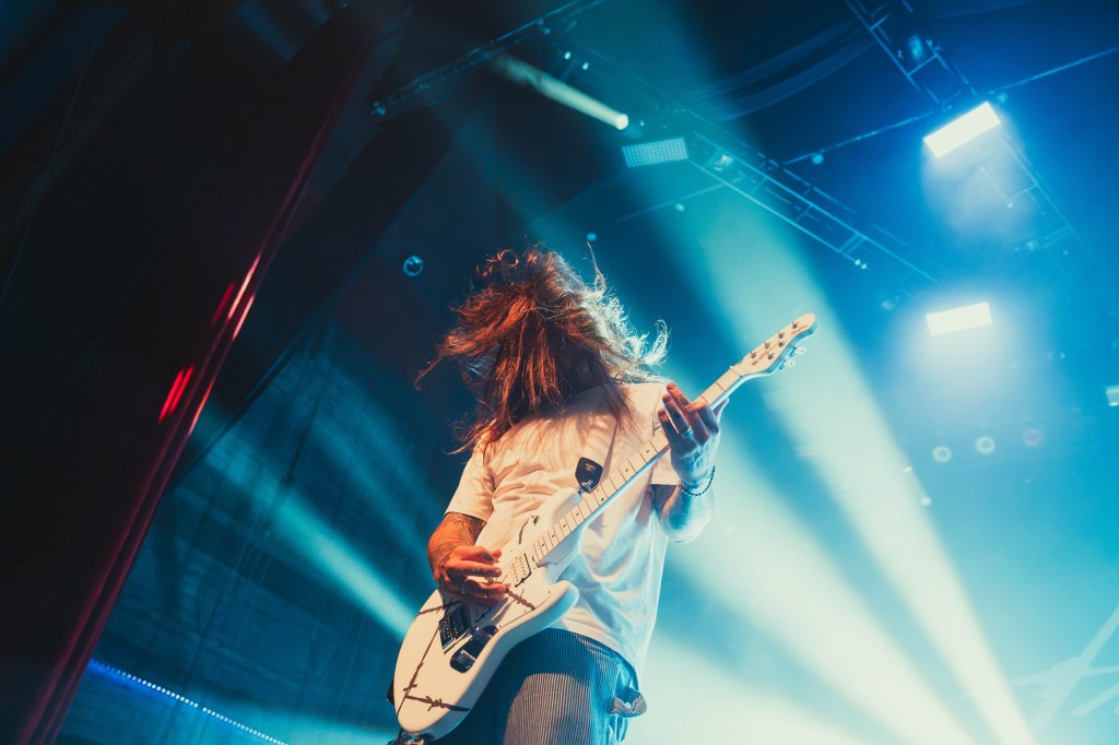 A musician passionately playing an electric guitar on stage, with dramatic lighting and hair flowing in motion.