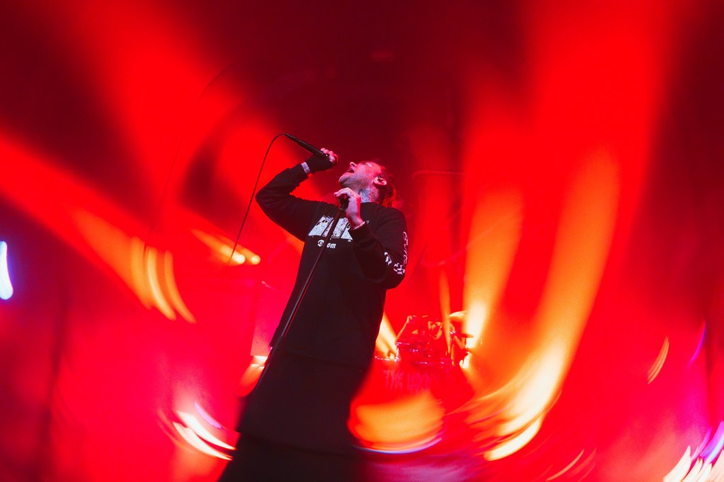 A singer passionately performing on stage with a microphone, surrounded by dramatic red lighting.